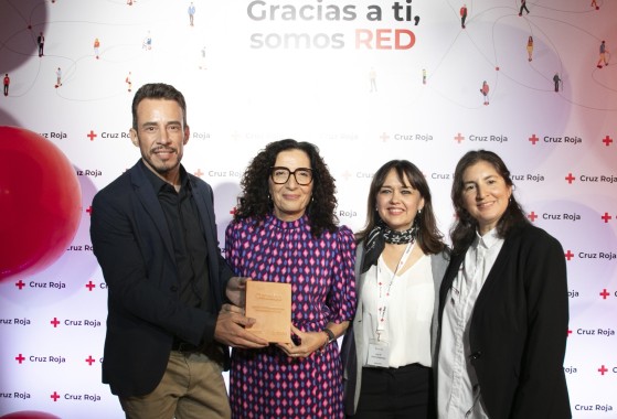 Cuatro personas, dos de ellas trabajadoras de GLS, posan en un evento de Cruz Roja. Una de las personas sostiene un reconocimiento frente a un fondo corporativo de Cruz Roja.