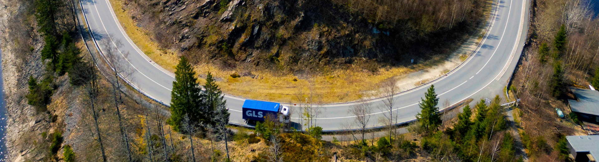 Camion semi-remorque GLS bleu sur une route de montagne en lacet, en milieu naturel.