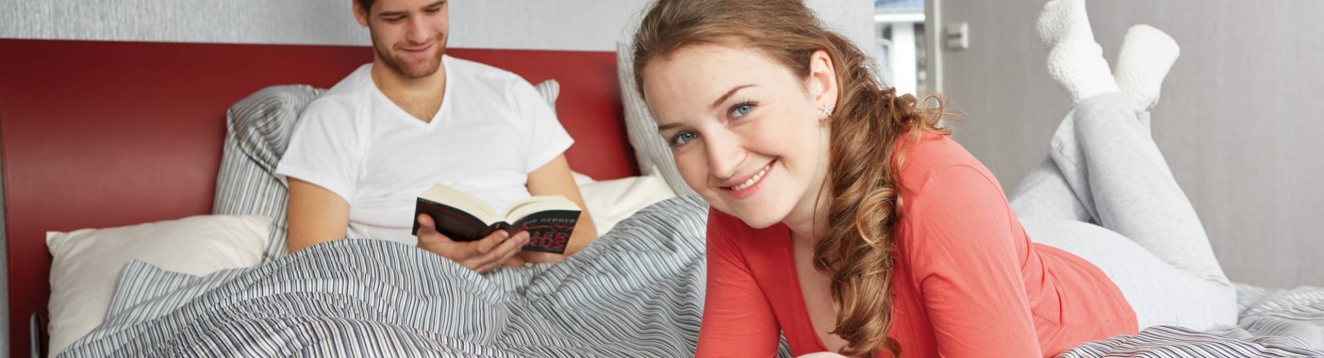 A man reading his book and a woman on her tablet in bed